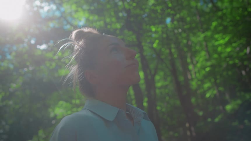 A woman is standing in a wooded area and smiling