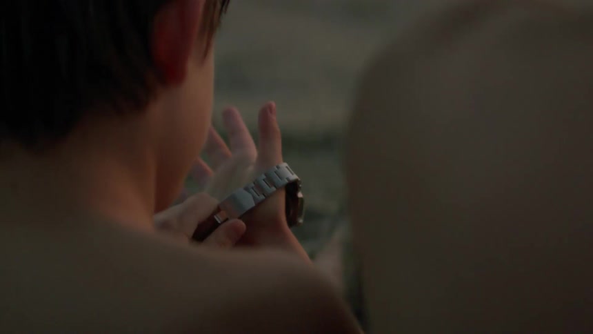 Son wears watch sittin next to father on the beach