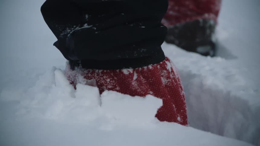 A close up of a persons feet in the snow wearing black and red clothing