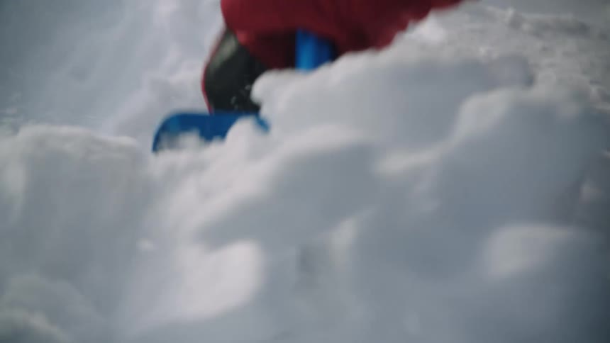 Man standing in snow covered fieldwith mountains in the background digs trench in snow