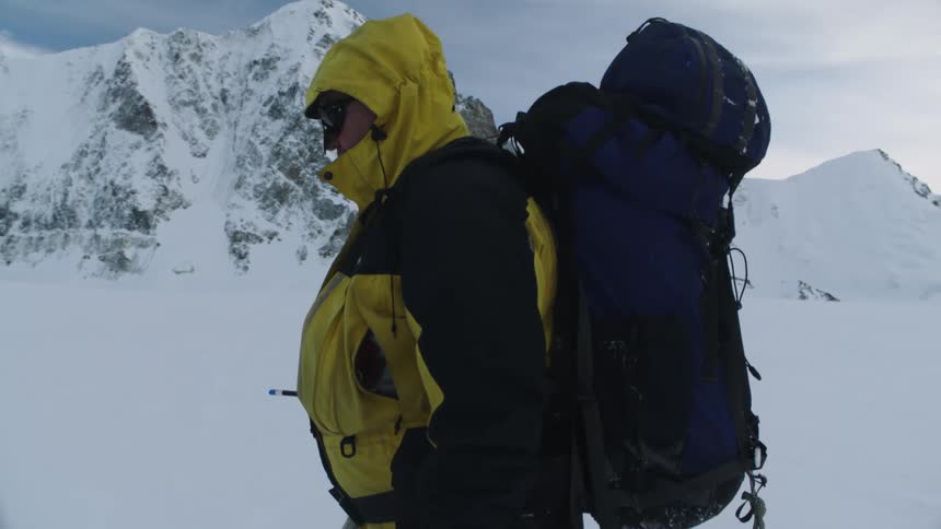Hiker with backpack yellow jacket and red gloves hikes through deep snow next to mountain