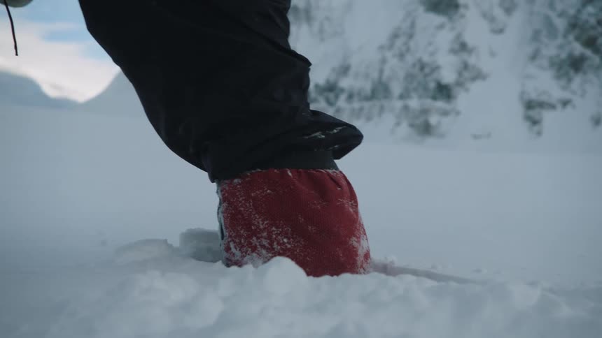 Man with black pants and red boots hikes through snow in the field