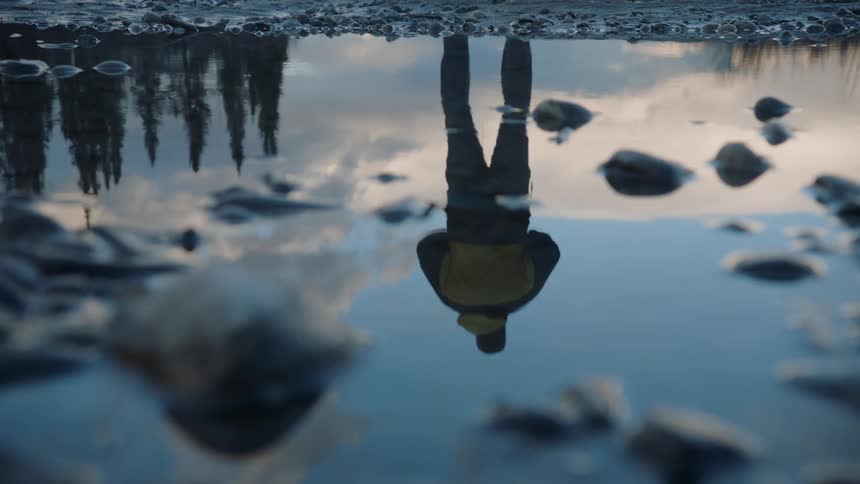 A mans reflection is shown while standing along a stream