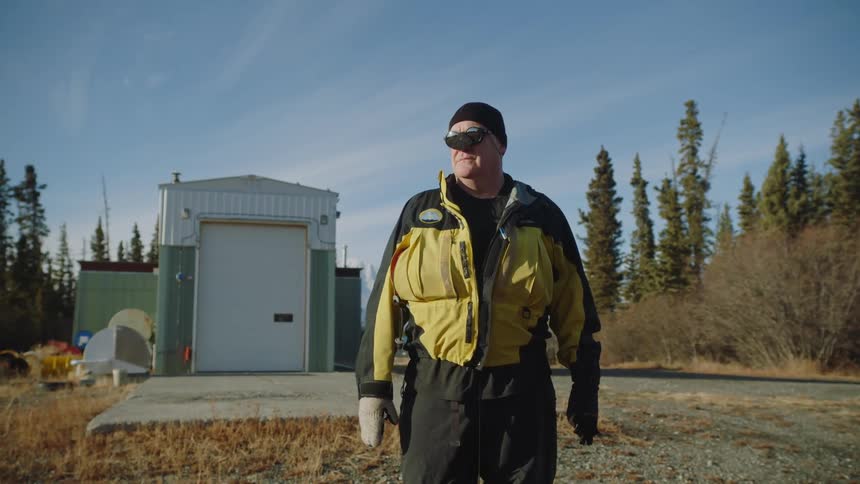 Man wearing winter clothes standing in front of a small structure in the forest at daytime