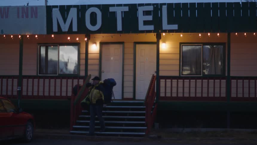 Man walking down steps of a motel carrying luggage at night