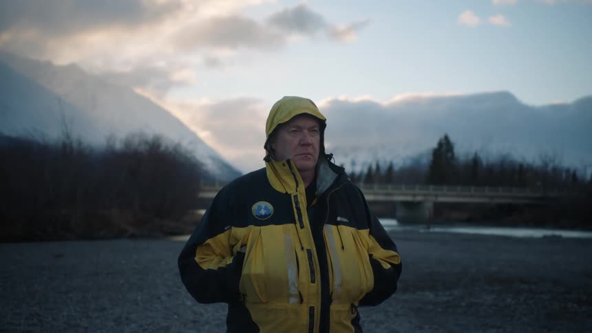 A man is standing outdoors in the wilderness at dusk