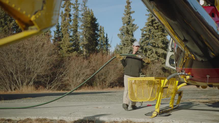 A man carrying a hose over to a helicopter and resting it on a yellow crate