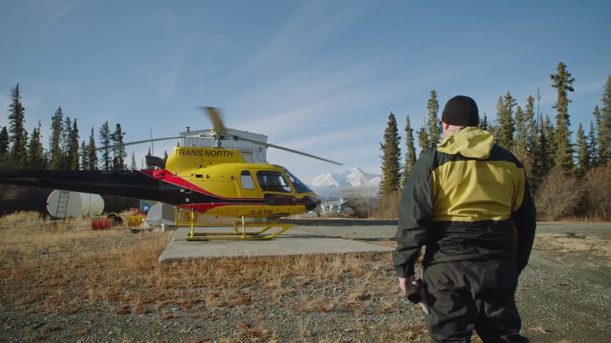 Man stands next to a helicopter that recently landed on a helipad in the mountains