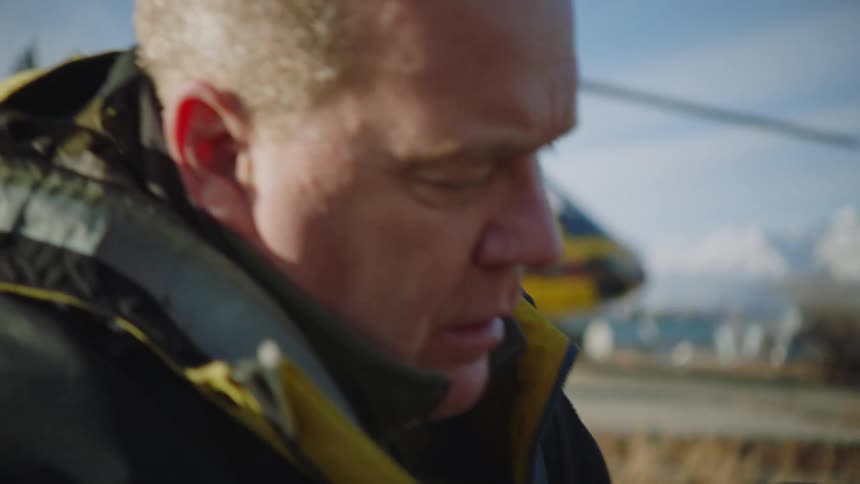 Mountains in the distance and a helicopter behind a man sitting on the ground moving around