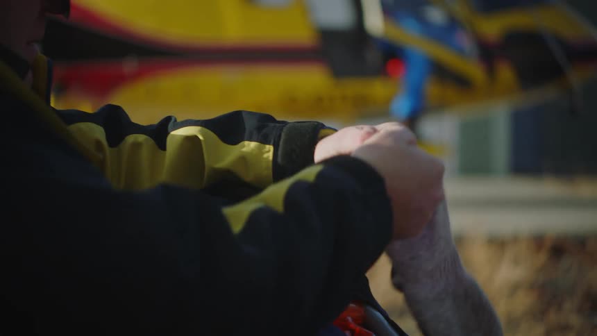 Man sitting outdoors with yellow helicopter in the background puts on gloves