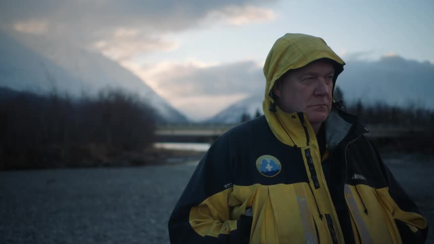 A man wearing a yellow and black coat standing looking angrily with his hood up