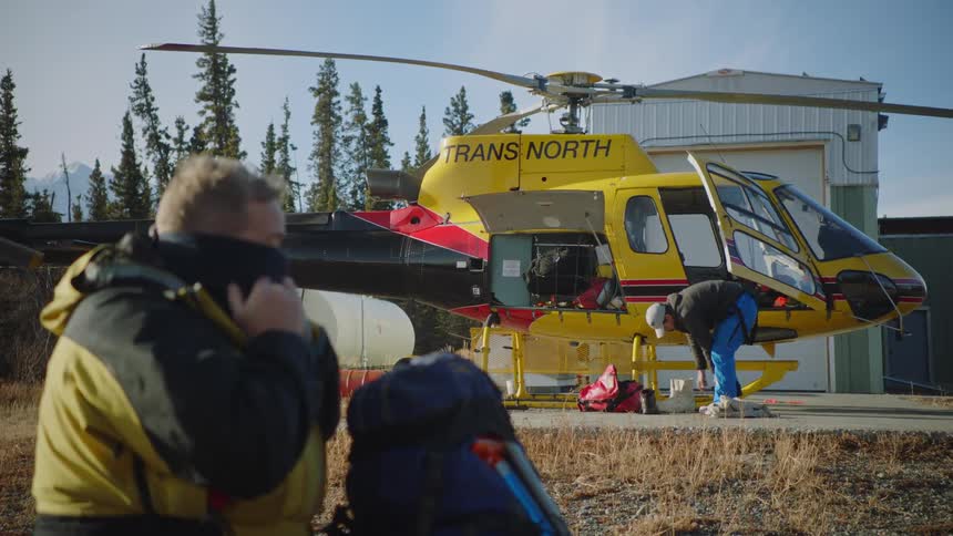 People gearing up for a mountaineering trip next to a helicopter on a helipad in the forest