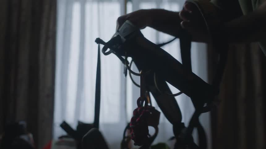 Man standing in dimly lit room straightens out a climbing harness