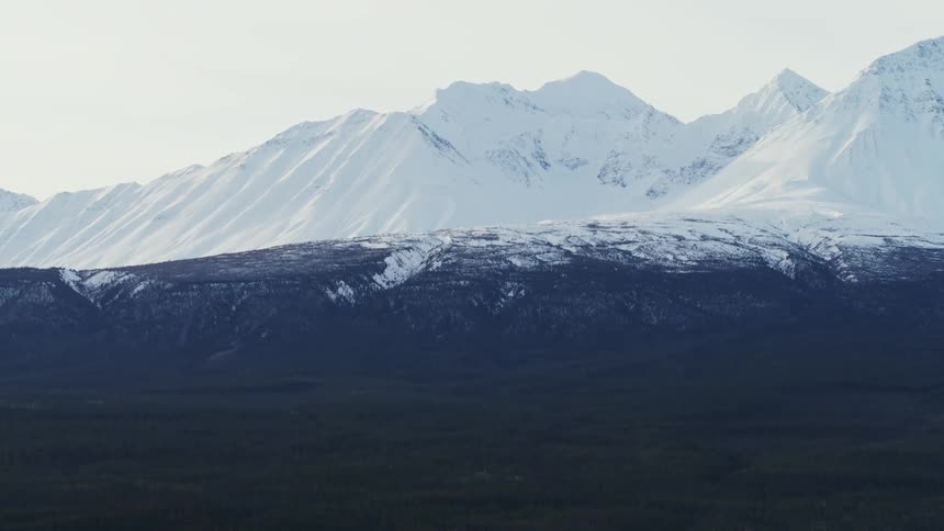 Snow dusts top of hill at base of snow covered mountains