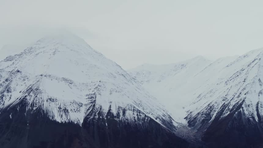 Snow covered mountains stand tall with peaks high in a hazy white sky