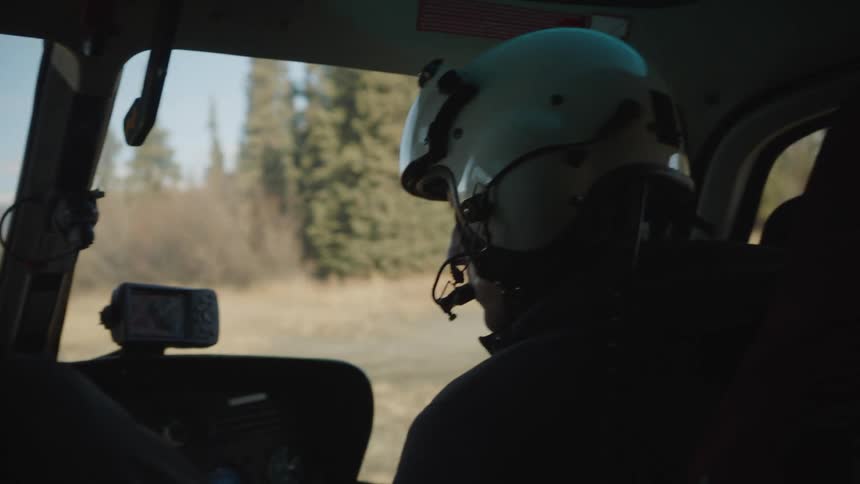 A person wears a headset and helmet as they look out the window of a vehicle