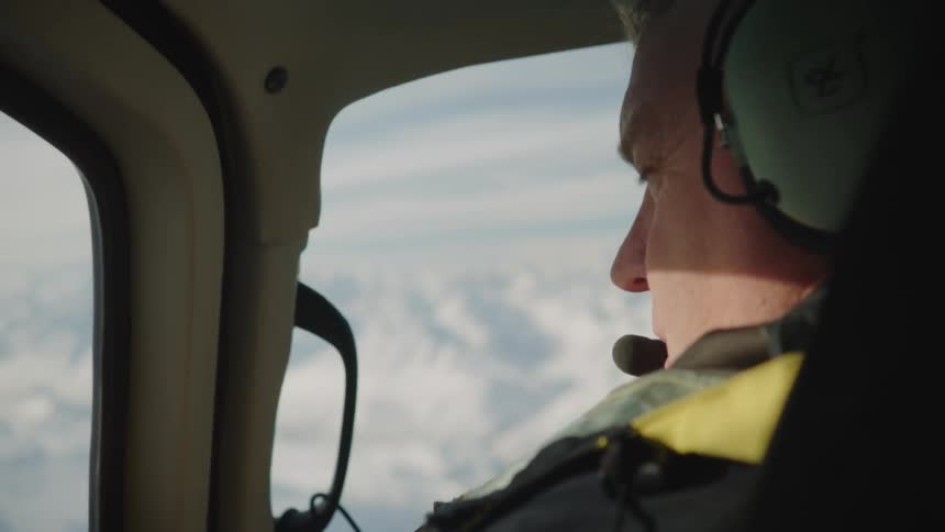 A man wearing a headset is flying a helicopter as he speaks into his microphone