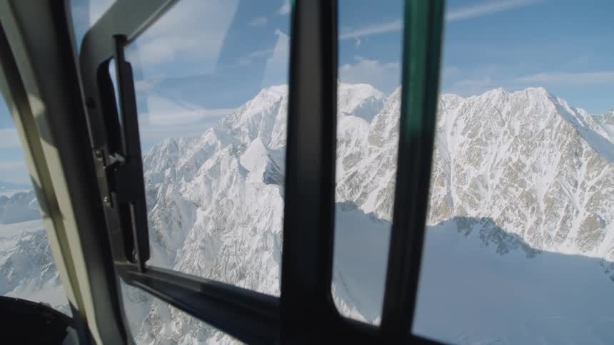 Snow covered mountains are seen through the window of an aircraft