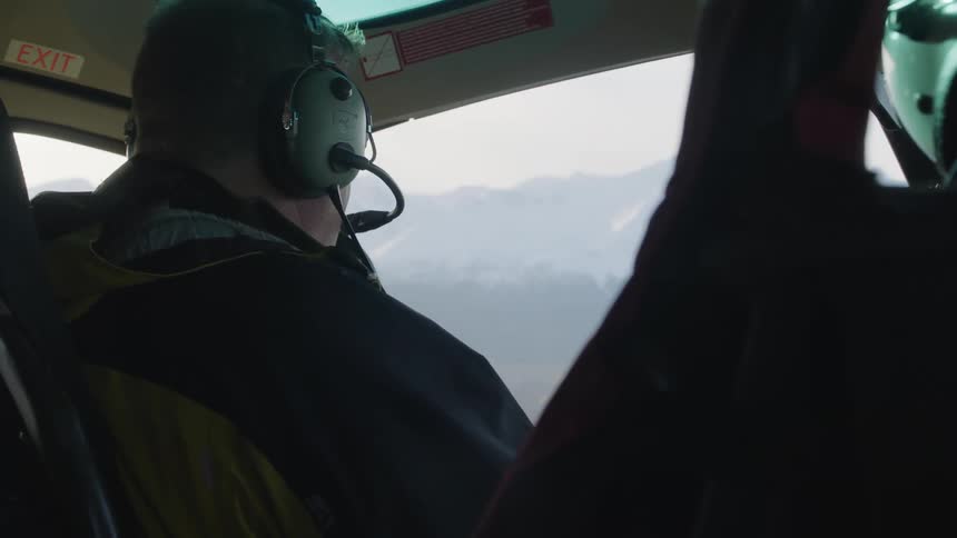 A man flying a helicopter wearing a head piece and talking to another person next to him