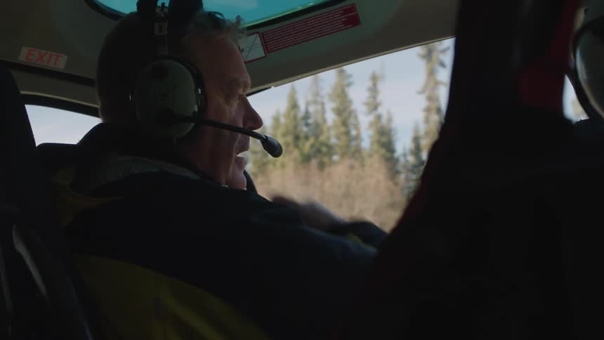 A man flying a helicopter talking to someone next to him while wearing a headset