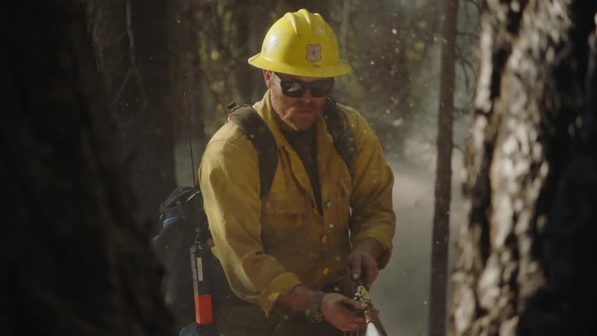 A man wearing a yellow hard hat uses a hose in the forest