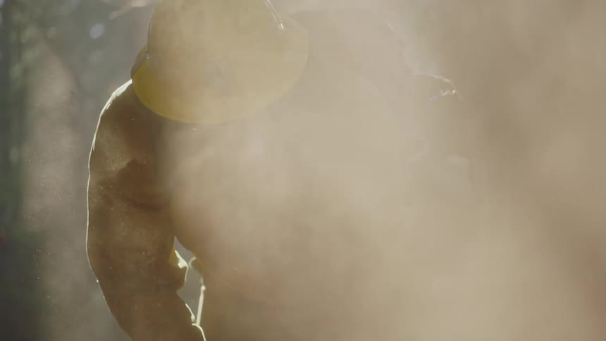 Firefighters wearing yellow protective gear rakes the ashes on the ground after a forest fire