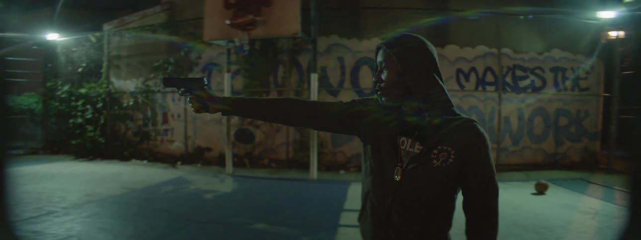 A man in a hoodie aims a gun on a basketball court