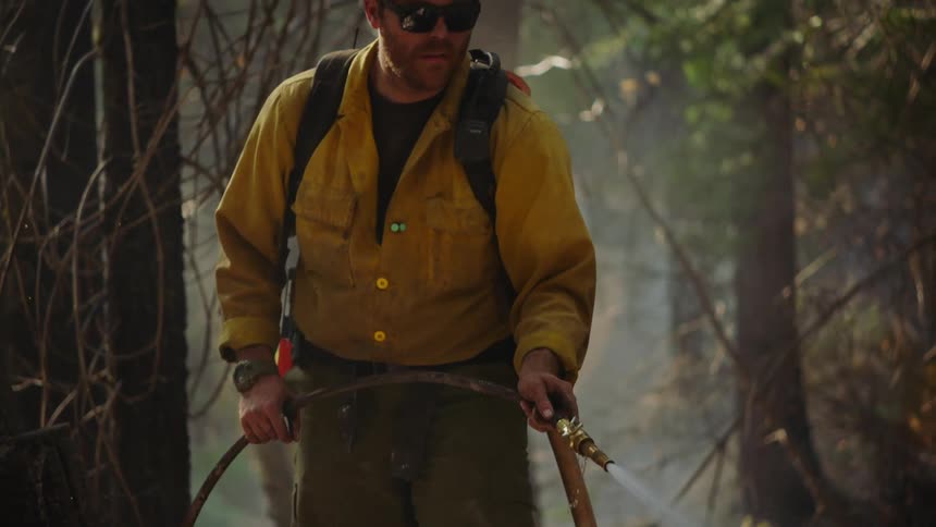 Firefighter sprays ground from water hose in smoky forest