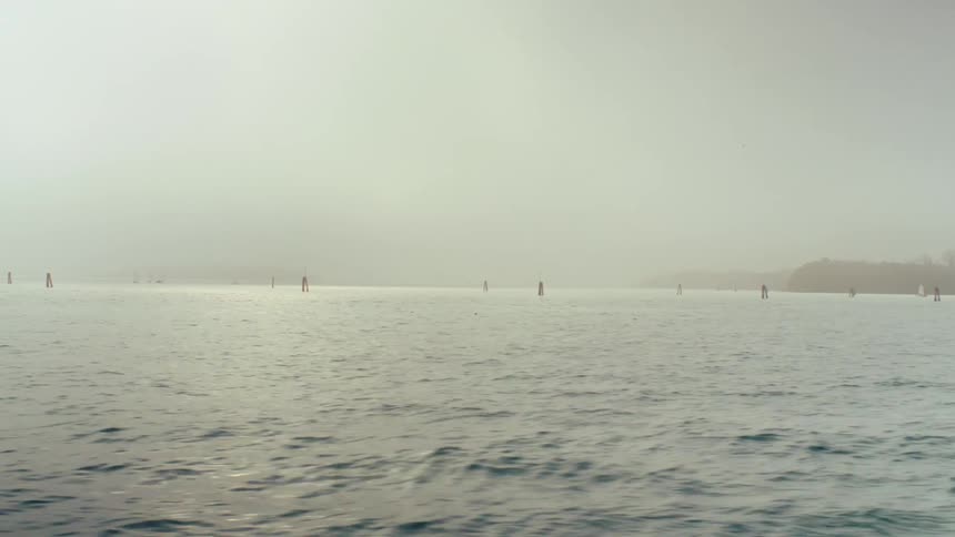 Rough ocean waters with poles in the water with lights on them and fog settled over the water
