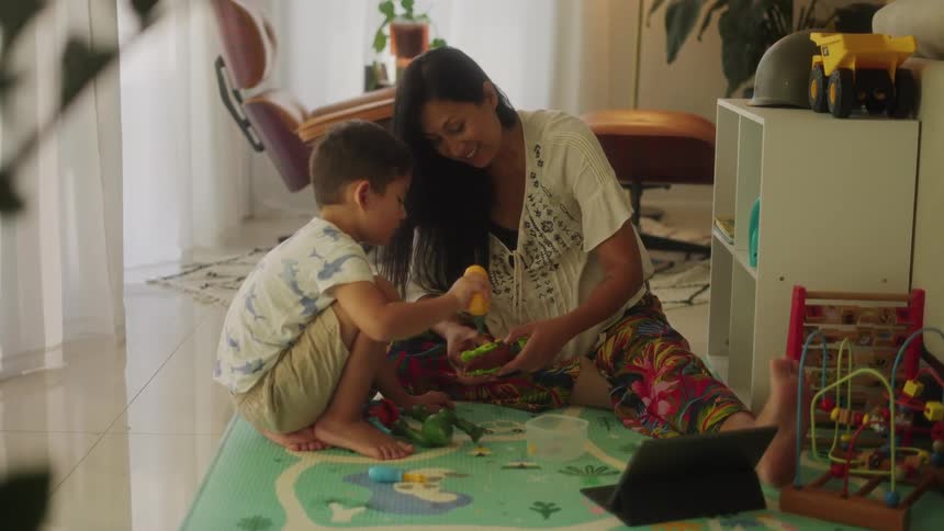 Mother and son sitting on the floor play with toys in the living room