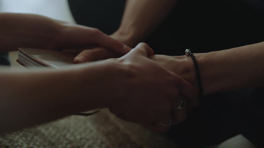 Close up of the trembling hands of a woman holding a book being held comfortingly by a friend