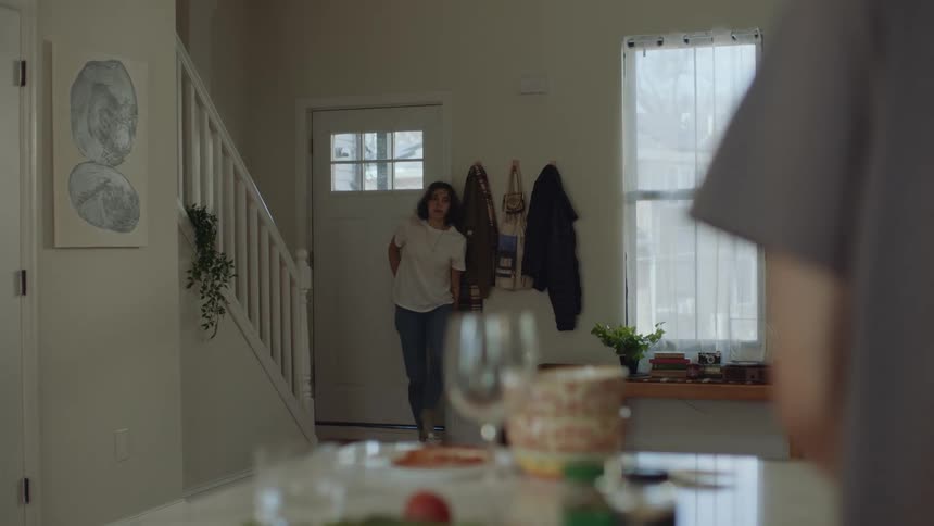 Young woman suddenly opens the front door of the house and enters walking slowly towards a man