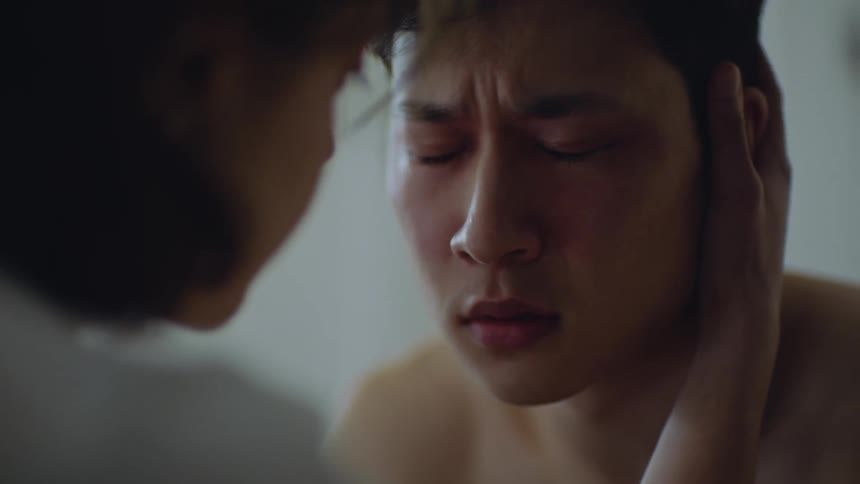 A close up of a mans face looking angry while another person puts her hand on his face