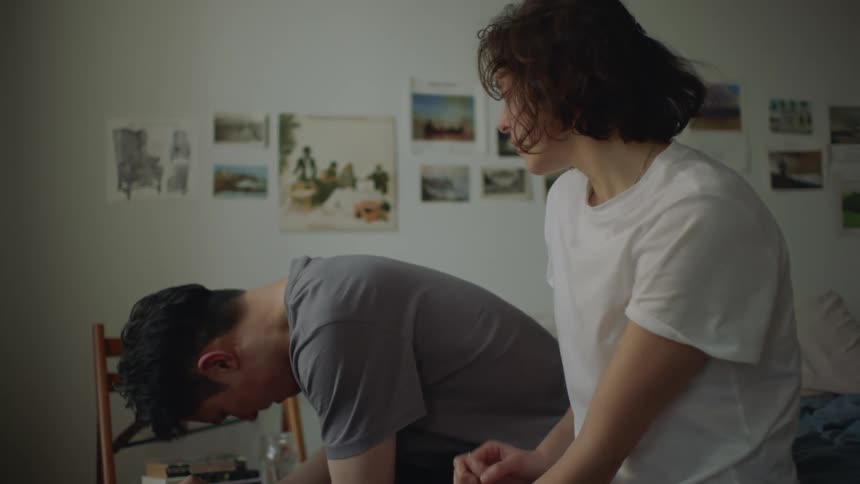 A man sitting on the edge of a bed with his head down as a woman walks over and sits next to him putt her hand on him then hugging him