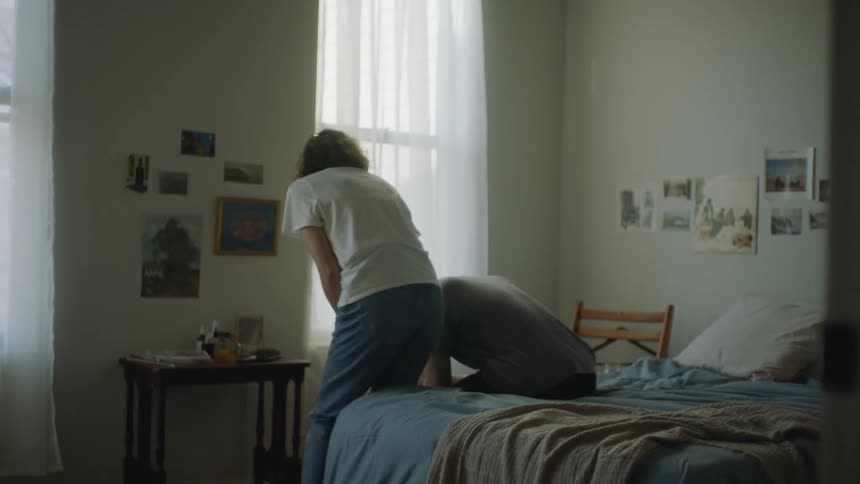 A man and woman sitting separately on a bed when the women walks over and sits next to the man