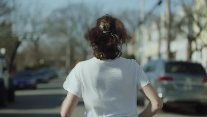 Woman with dark hair white shirt and jeans runs down the street in the city