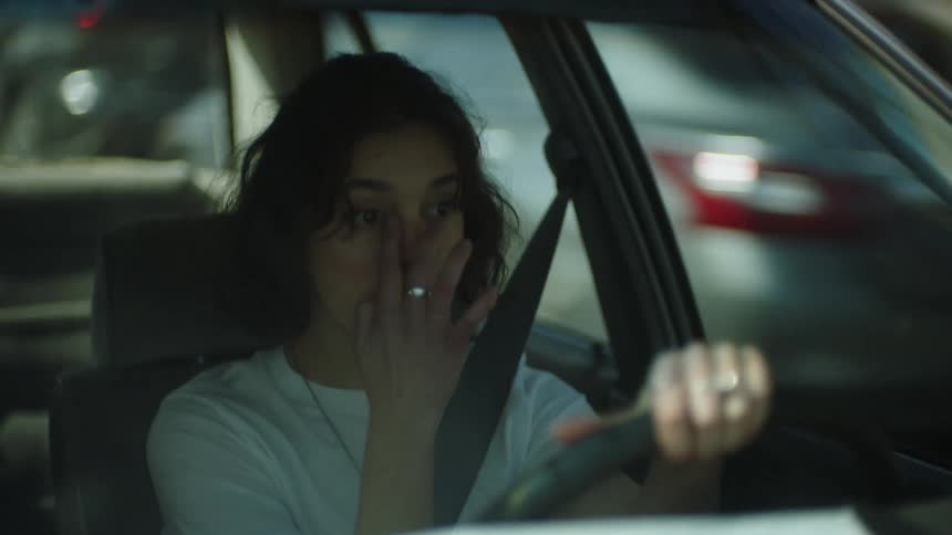 A tired woman drives a car along a roadway during the day