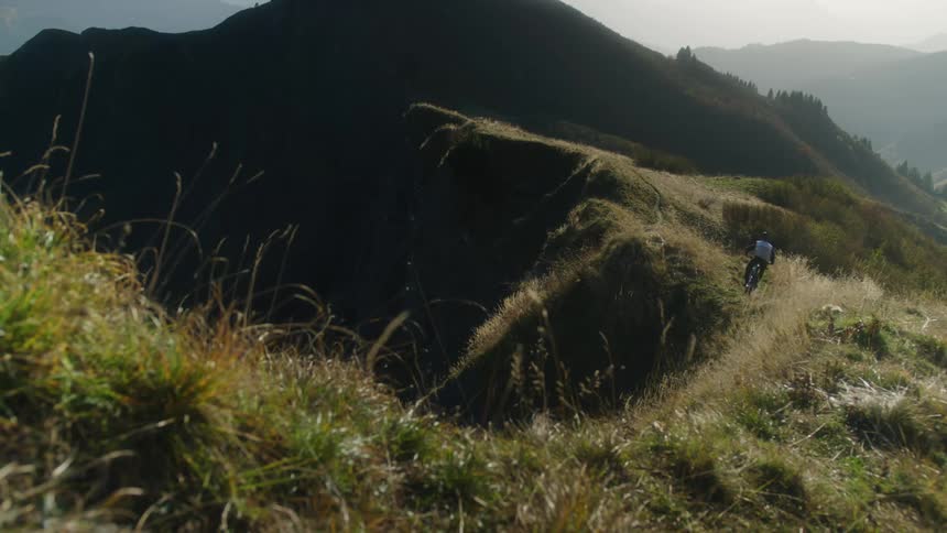 Man riding a bicycle over the ridge of a mountain at morning at full speed