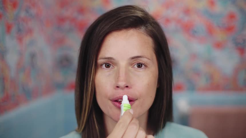 Woman with brown hair and light blue shirt applies lipstick