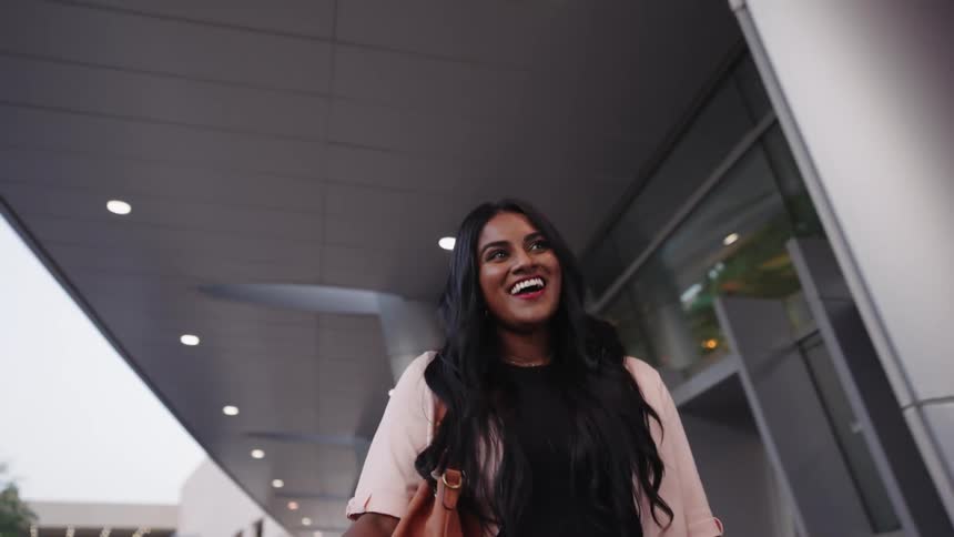 A woman is walking outside of a modern looking building and smiling