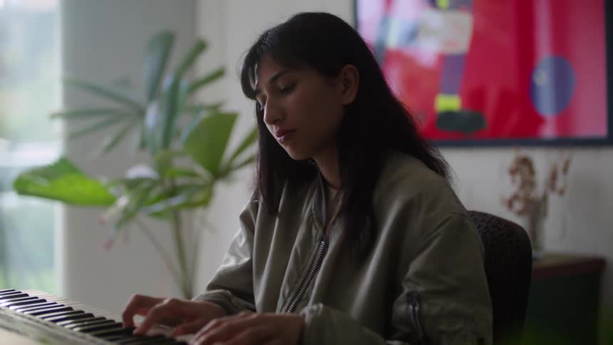 A young woman plays a musical keyboard while sitting indoors during the day