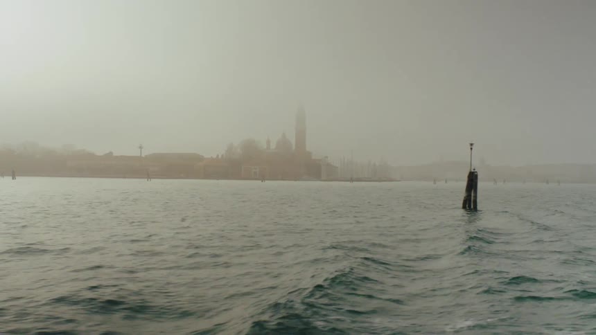 Mooring posts form a line a distance from foggy town on coast