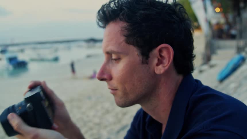 Man in dark blue shirt takes photo with camera on the beach