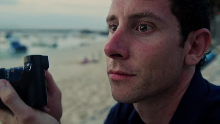 Man in dark black shirt takes photo with camera on the beach at sunset