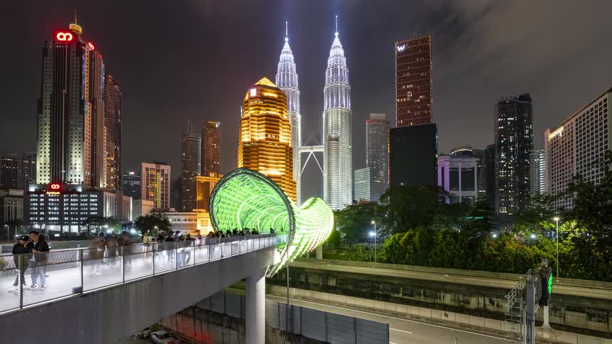 A time lapse view of Kuala Lumpur city skyline with towers and a busy bridge tunnel lit up in neon lighting