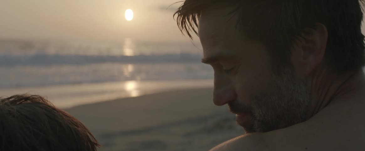 Loving father sitting on the beach at sunset turns around to look at his son