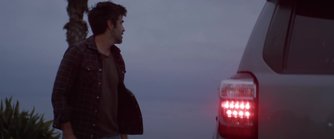 A man is getting out of his parked car at dusk