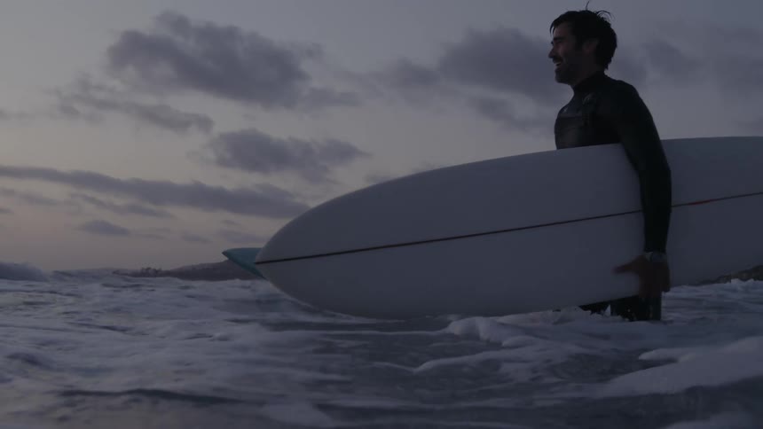 Father and son in wetsuit carrying surfboards into sea at sunset