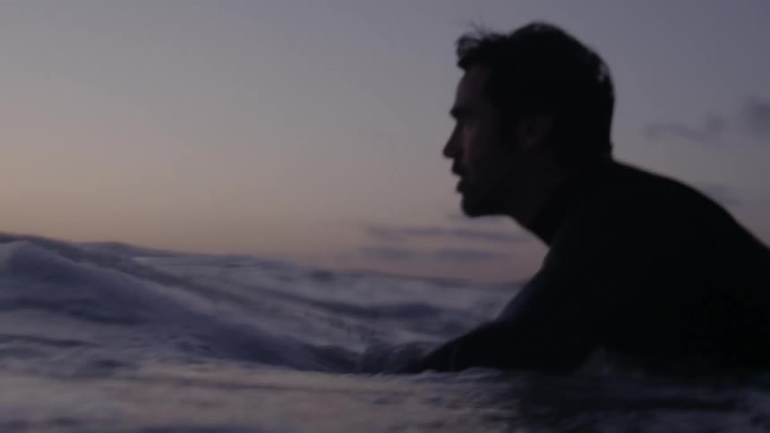 A man is surfing in the ocean water at dusk