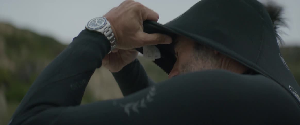 Man with beard and silver wristwatch wears wetsuit on the beach